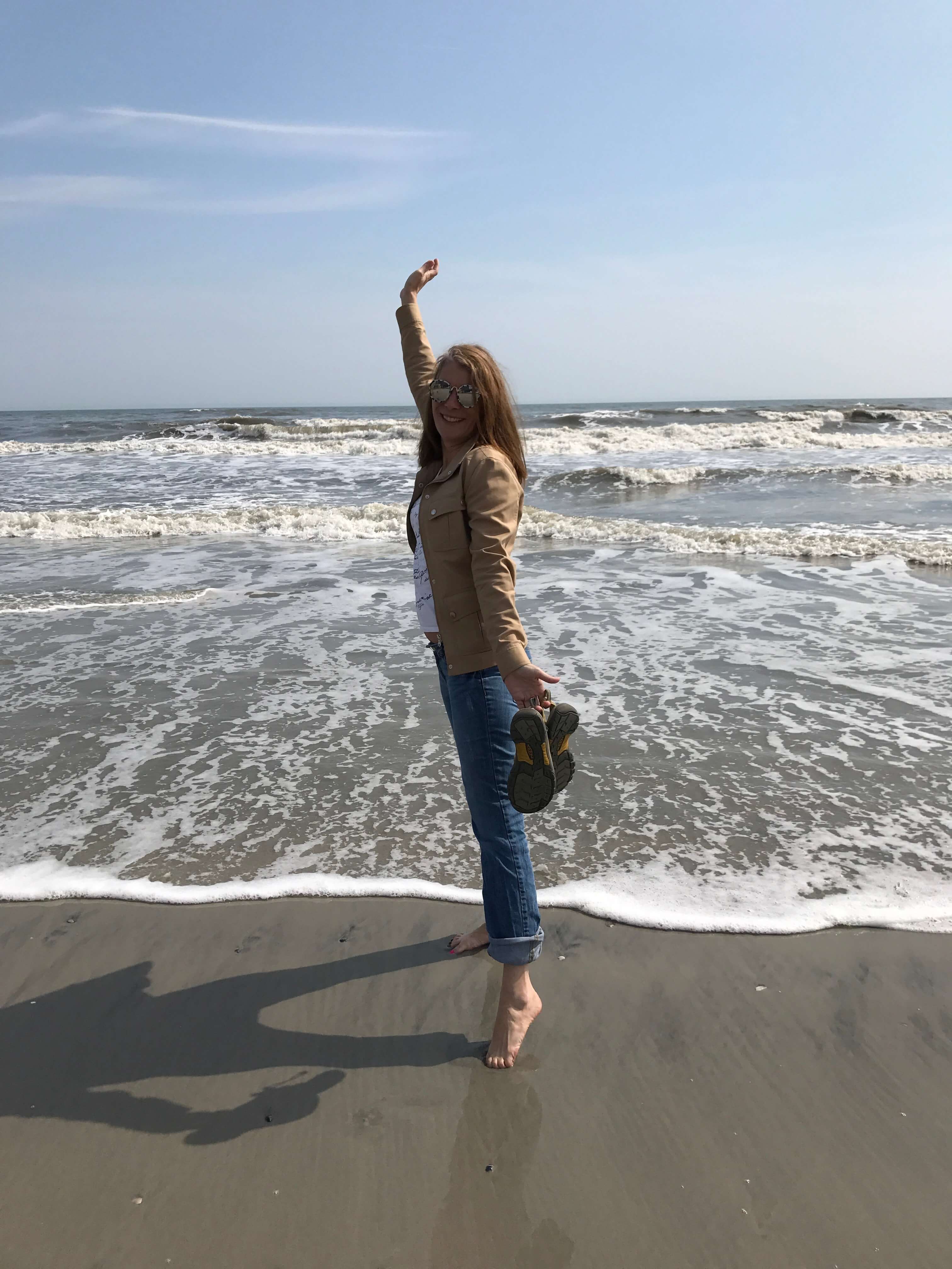 Audrey standing at the beach on tippy toes waving