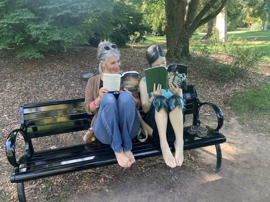 art themed book club adventure by the woman sitting on bench reading a book next to a sculpture of a women sitting on the same bench reading a book 